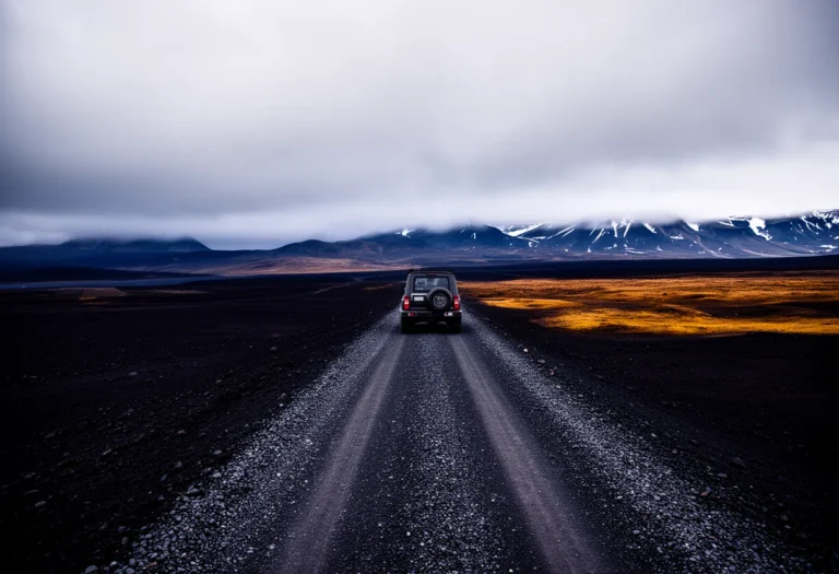 Single vehicle on a gravel road crossing a black volcanic plain in Iceland under low cloud