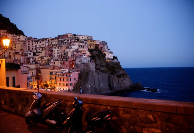 Cliffside Italian coastal town at dusk with parked scooters on a terrace above a dark blue sea